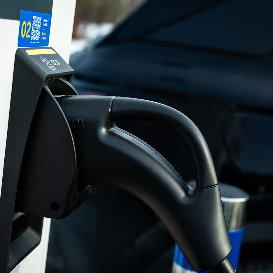 Tuvplāns elektriskā transportlīdzekļa lādētājam ar zilu uzlīmi “Skenēt un uzlādēt”.