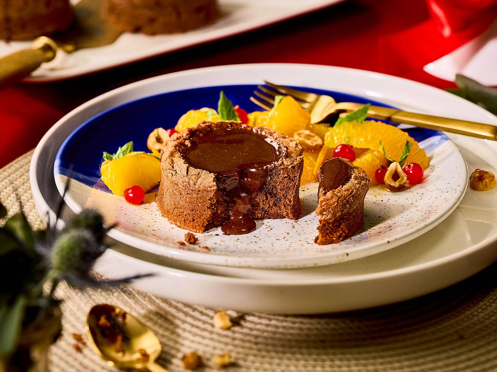 Šokolādes fondants ar apelsīnu šķēlītēm, sarkanajām jāņogām un lazdu riekstiem uz šķīvja.