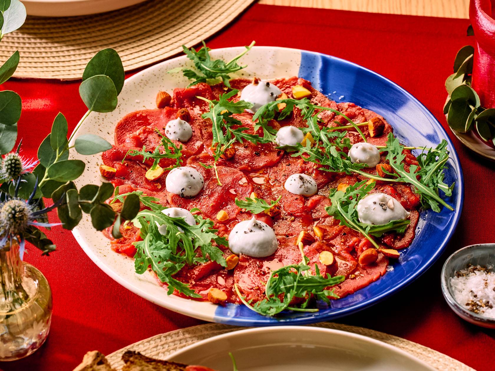 Biešu karpačo ar rukolu, mandelēm un sieru uz zili-balta šķīvja.