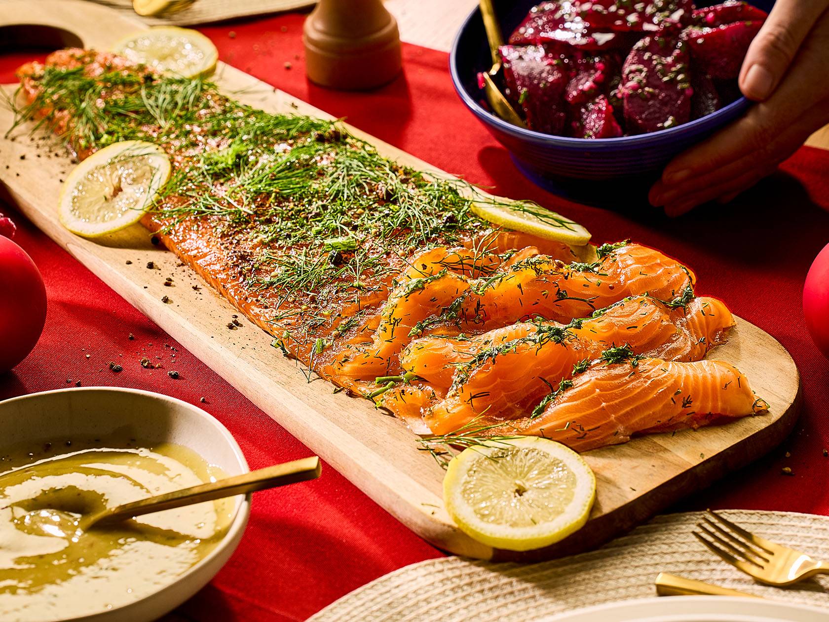 Laša gravlakss ar dillēm un citronu uz koka dēļa, blakus mērce un biešu salāti.